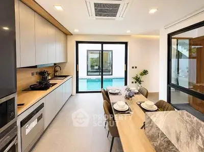 Modern kitchen with open layout and pool view, featuring sleek cabinetry and elegant dining setup.