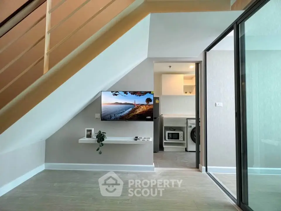 Modern interior with TV under staircase and glass partition leading to laundry area.