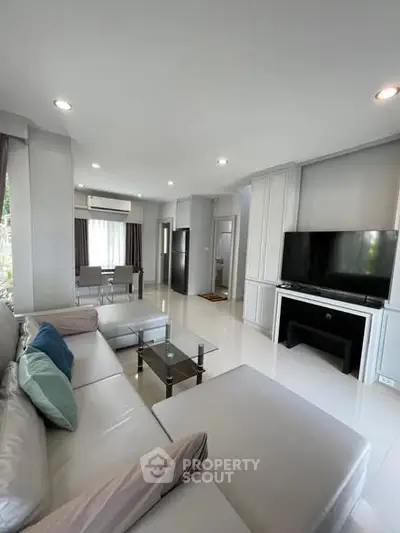 Spacious modern living room with sleek furniture and large TV, perfect for relaxation.