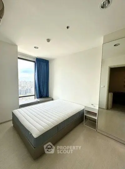 Spacious bedroom with large window offering city views, featuring a comfortable bed and modern decor.