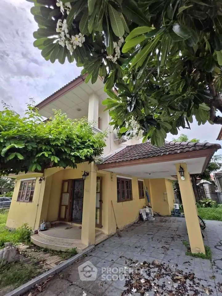 Charming two-story yellow house with lush greenery and tiled patio, perfect for family living.