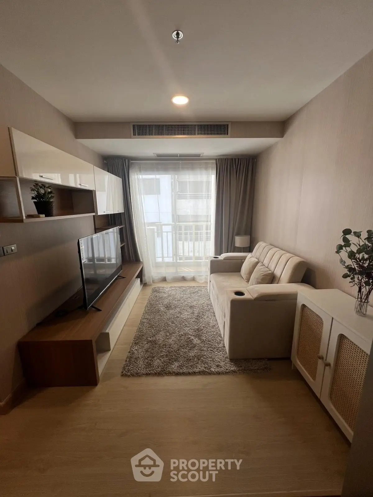Cozy modern living room with plush sofa, stylish TV unit, and natural light from large window.