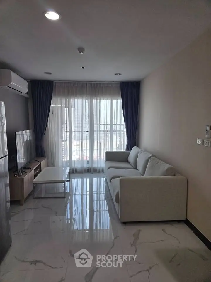 Modern living room with sleek sofa and large window offering natural light and city view.