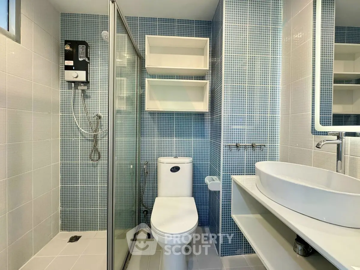 Modern bathroom with glass shower, sleek fixtures, and blue mosaic tiles.