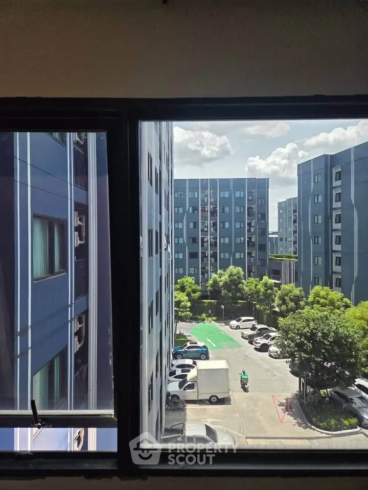 Stunning view from window overlooking modern apartment complex and lush greenery.