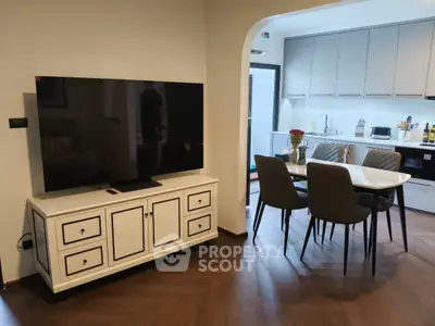 Modern living room with sleek kitchen and dining area, featuring a large TV and stylish furniture.