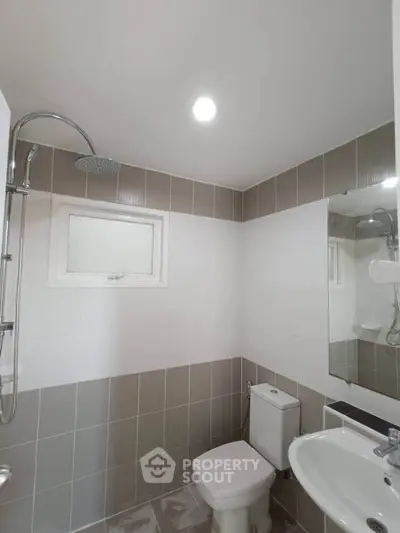 Modern bathroom with sleek fixtures and neutral tiles, featuring a shower and toilet.