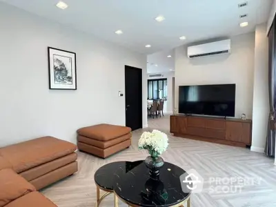 Modern living room with stylish furniture and large TV, open layout to dining area.