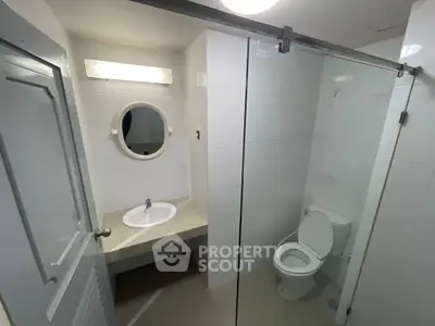 Modern bathroom with glass shower and round mirror in sleek white design.