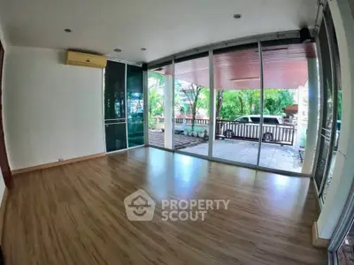 Spacious living room with large windows and wooden flooring, offering a serene view of the garden.