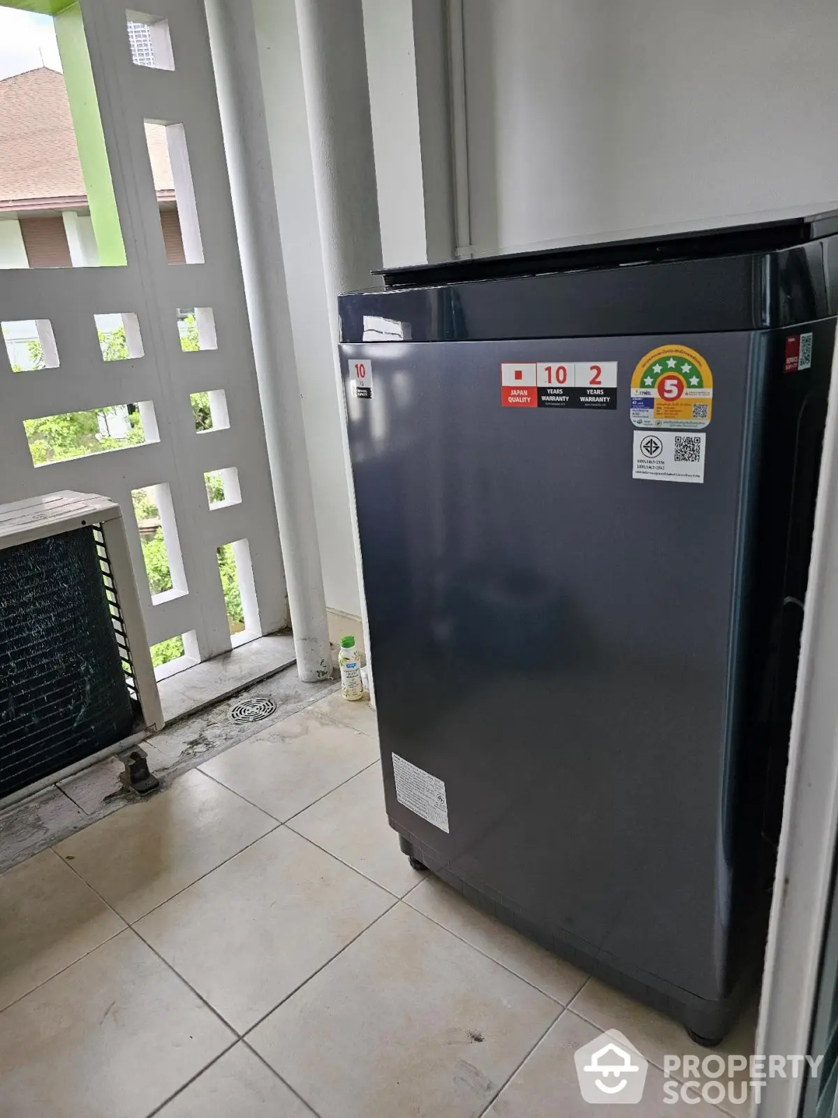 Modern washing machine on tiled balcony with partial view of greenery.