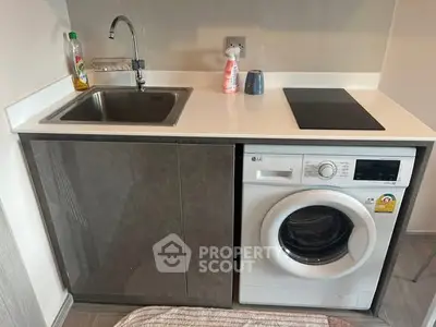 Compact kitchen with sink, washing machine, and electric cooktop in modern apartment.
