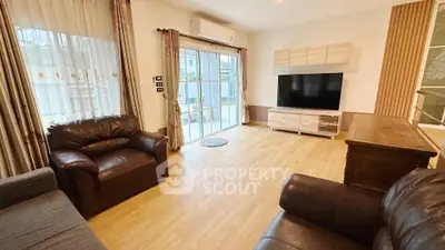Spacious living room with modern furniture and large TV, featuring natural light from sliding glass doors.