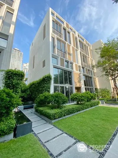 Luxurious modern building exterior with lush green garden, large windows, and elegant architectural design, nestled in a serene urban environment.