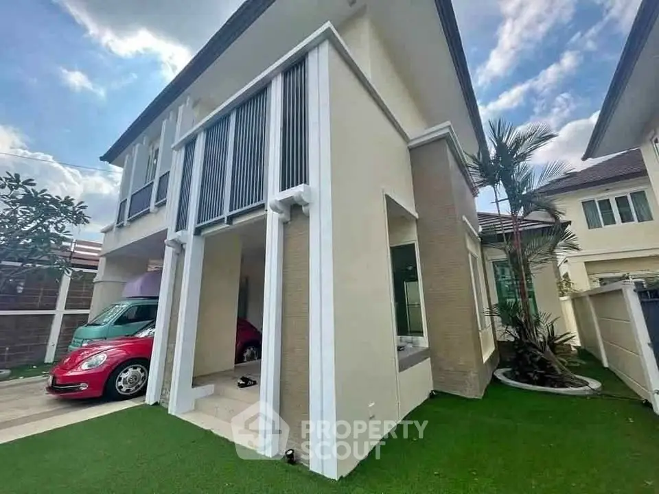 Modern two-story house with sleek design and lush green lawn, featuring a red car parked in the driveway.