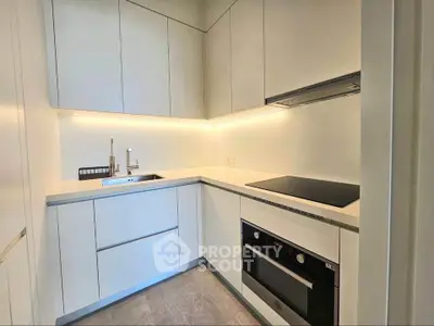 Modern kitchen with sleek white cabinetry and built-in oven, featuring under-cabinet lighting.
