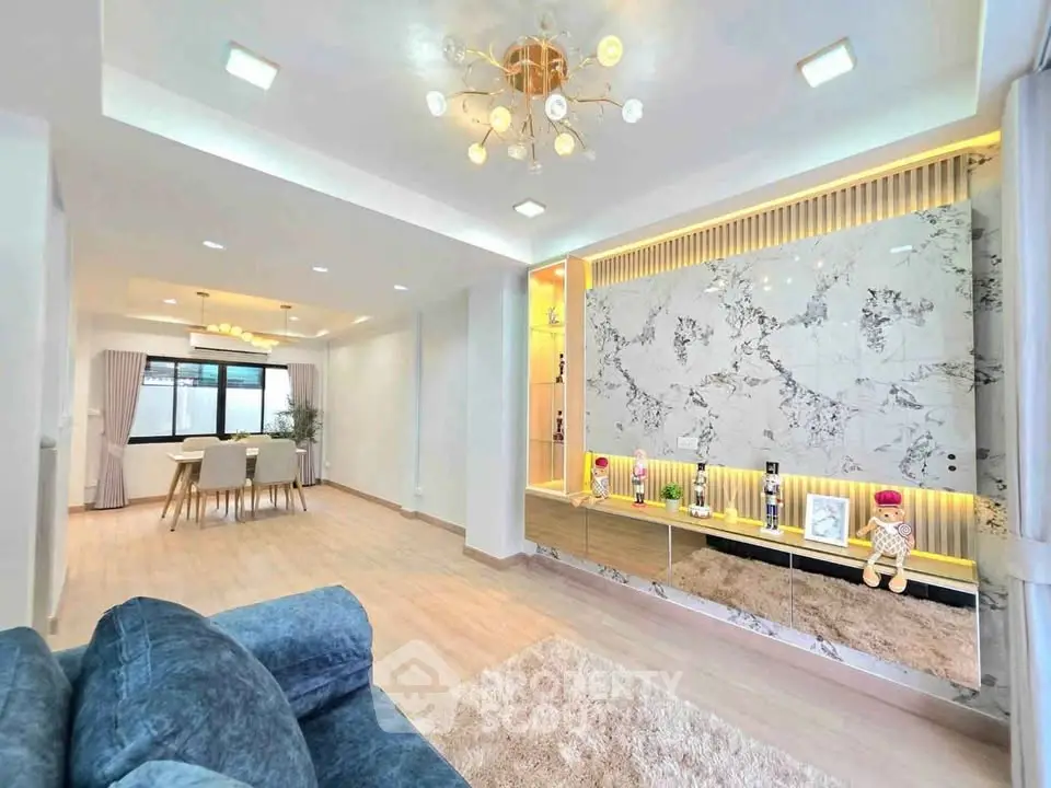 Spacious modern living room with elegant decor and open dining area, featuring stylish lighting and plush furnishings.