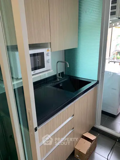 Compact modern kitchen with sleek cabinetry and built-in microwave, featuring a sliding glass door for space efficiency.