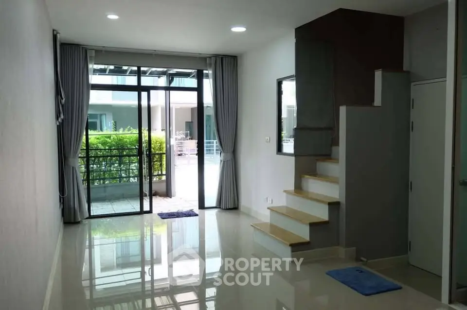 Spacious modern living room with large windows and garden view, featuring sleek staircase and glossy floors.