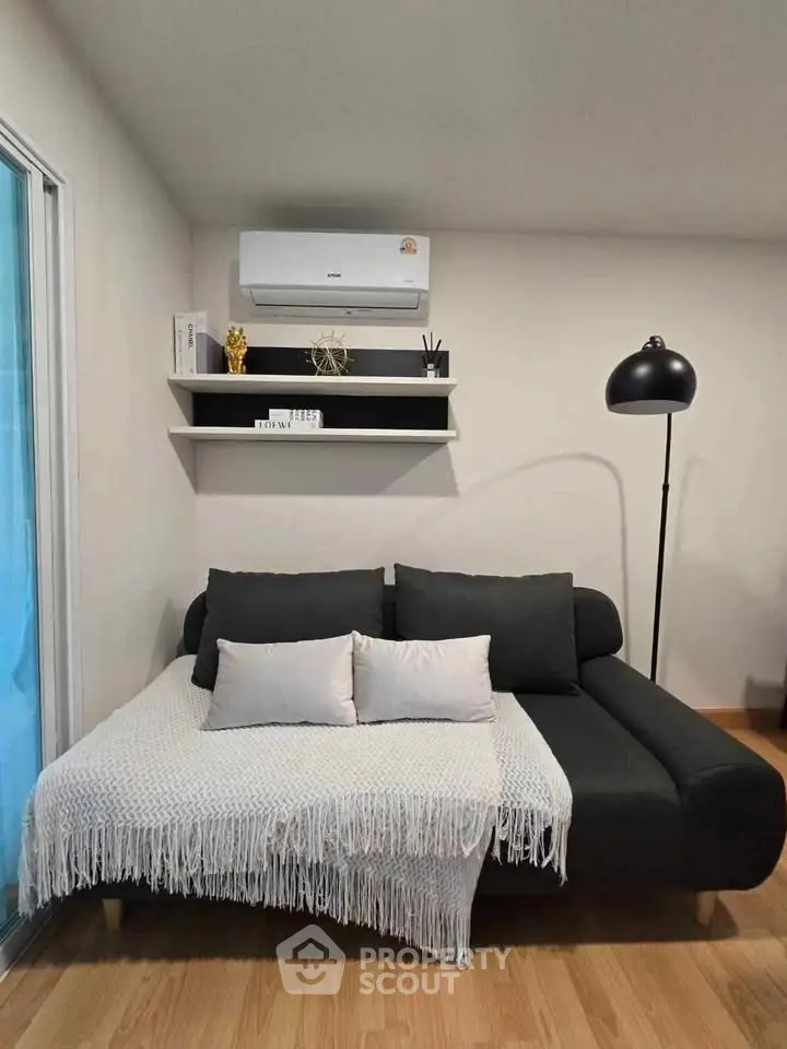 Modern living room with sleek black sofa, cozy throw, and stylish decor in a contemporary apartment.