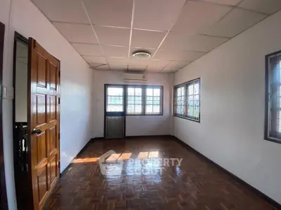Spacious empty room with wooden flooring and large windows, perfect for customization.