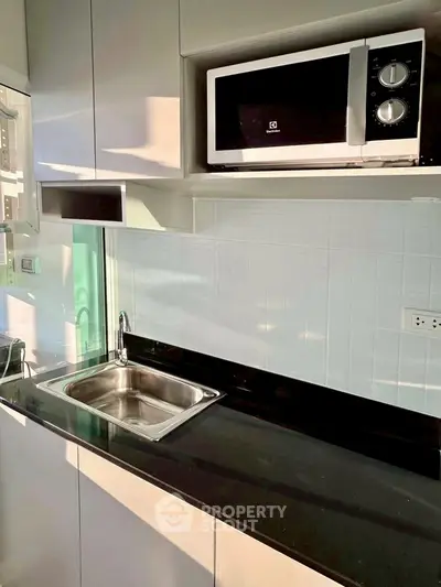 Modern kitchen with sleek cabinetry, built-in microwave, and stainless steel sink.