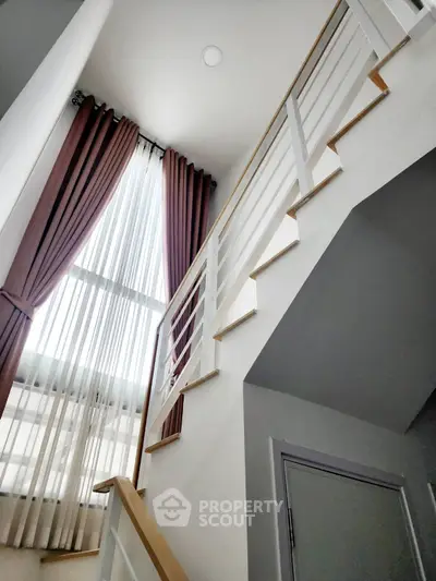 Modern staircase with tall windows and elegant curtains in a stylish home interior.