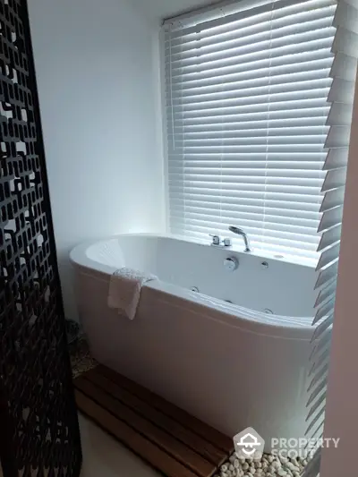 Luxurious corner bathtub with hydro jets, surrounded by elegant pebble detailing and modern privacy blinds, perfect for a spa-like experience at home.