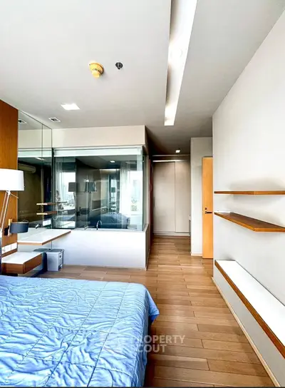 Modern bedroom with wooden flooring and glass partition, featuring sleek shelves and contemporary design.