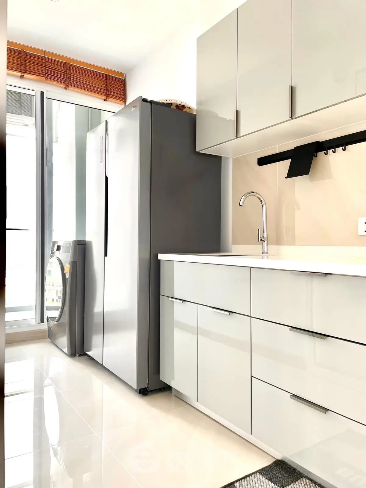Modern kitchen with sleek cabinets, stainless steel fridge, and washing machine in bright apartment.