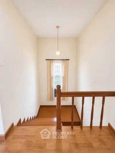 Charming staircase with wooden railing and natural light from window, perfect for cozy home ambiance.
