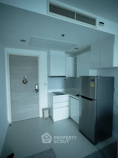 Modern compact kitchen with sleek white cabinets and stainless steel fridge in a stylish apartment.