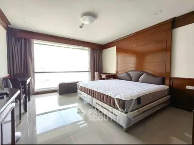 Spacious bedroom with large window and elegant wooden paneling, offering abundant natural light and serene ambiance.