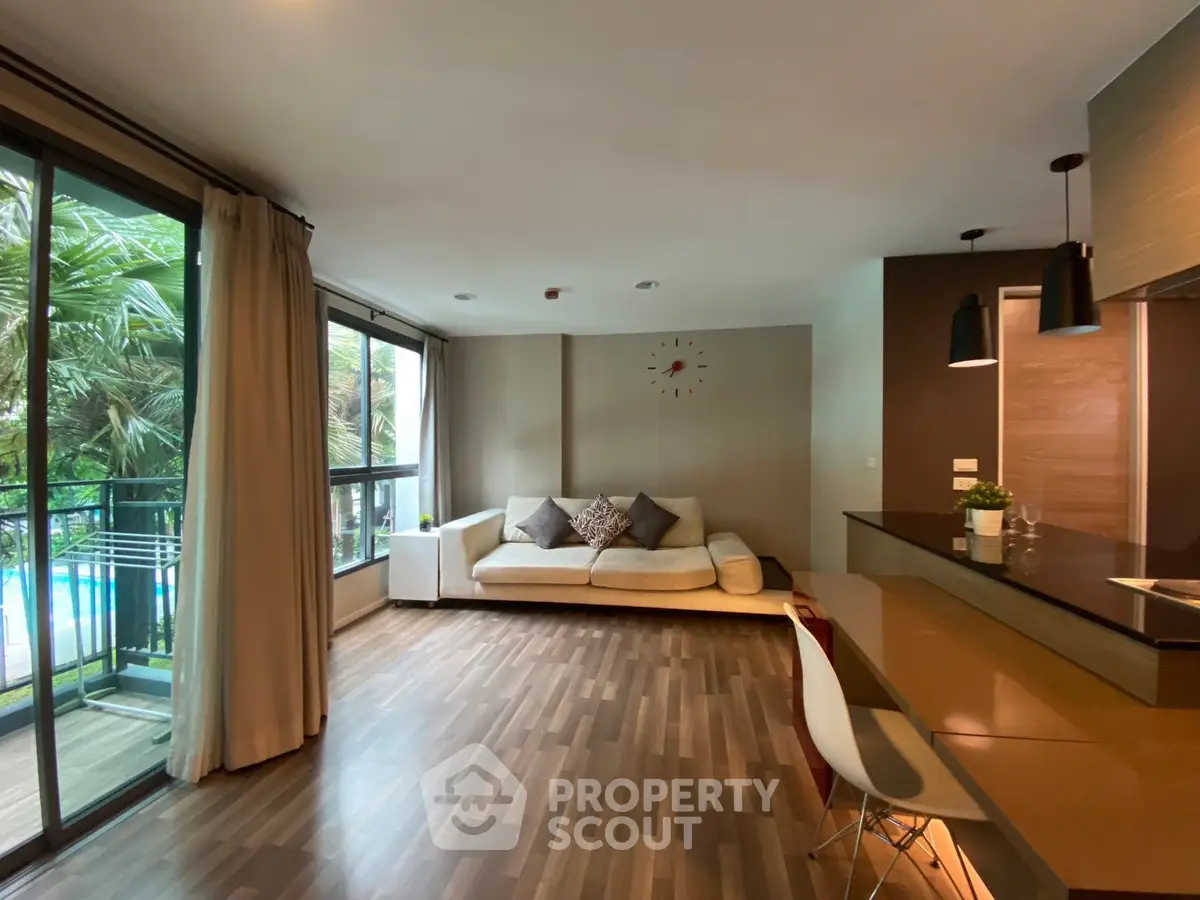 Spacious modern living room with large windows and balcony overlooking lush greenery.