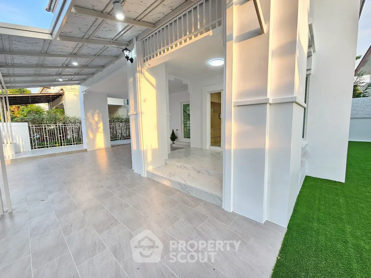 Elegant modern home entrance with spacious tiled patio and lush green lawn