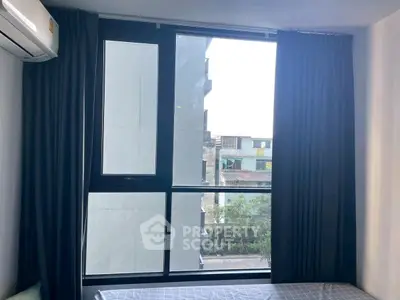 Modern bedroom with large window and city view, featuring dark curtains and air conditioning.