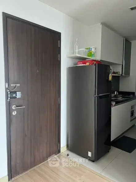 Modern kitchen with sleek fridge and wooden door, compact yet stylish design.