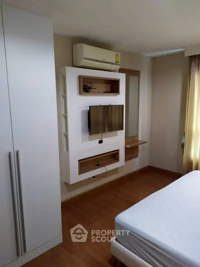 Modern bedroom with wall-mounted TV and air conditioning, featuring sleek storage solutions and wooden flooring.