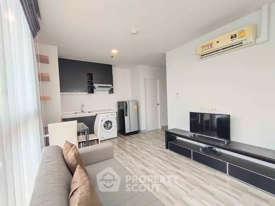 Modern living room with open kitchen, featuring a washing machine and sleek black furniture.