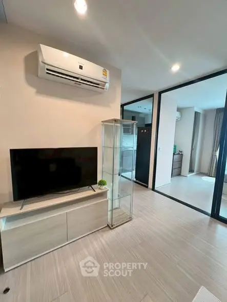 Modern living room with sleek TV stand and glass cabinet, featuring air conditioning and open layout.
