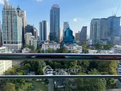 Stunning cityscape view from a high-rise balcony overlooking lush greenery and modern skyscrapers.