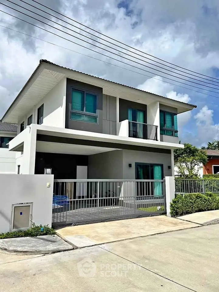 Modern two-story house with balcony and gated driveway in a suburban neighborhood.