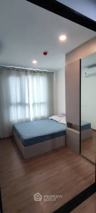 Cozy modern bedroom with large window and mirrored wardrobe in stylish apartment.
