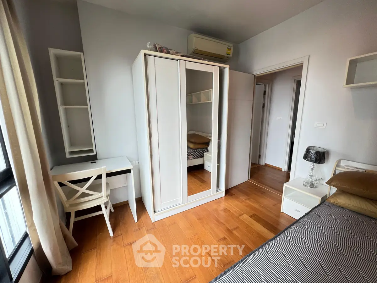 Charming bedroom with wooden flooring, white furniture, and ample natural light from large windows.