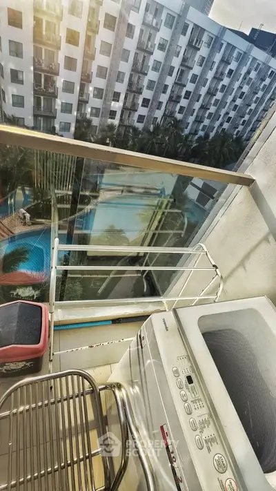 Modern balcony with washing machine and pool view in urban apartment complex.