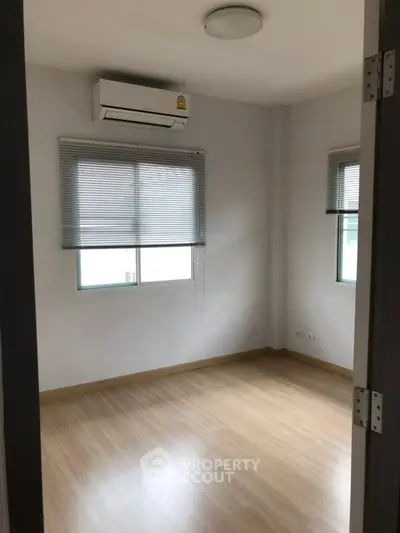 Bright empty room with wooden flooring and air conditioning unit.