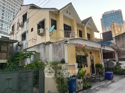 Charming two-story house with urban backdrop, featuring a small garden and satellite dish.