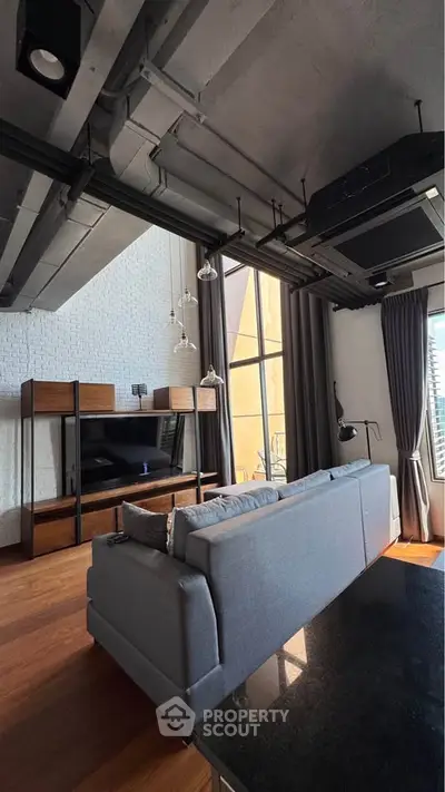 Modern living room with high ceiling and large windows, featuring stylish furniture and industrial design elements.
