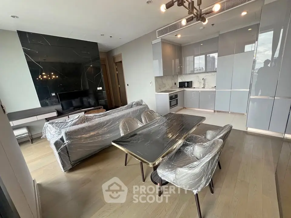 Modern open-plan living room with sleek kitchen and dining area, featuring stylish furniture and natural light.