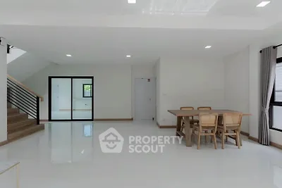Spacious modern living room with dining area and staircase, featuring minimalist design and natural light.
